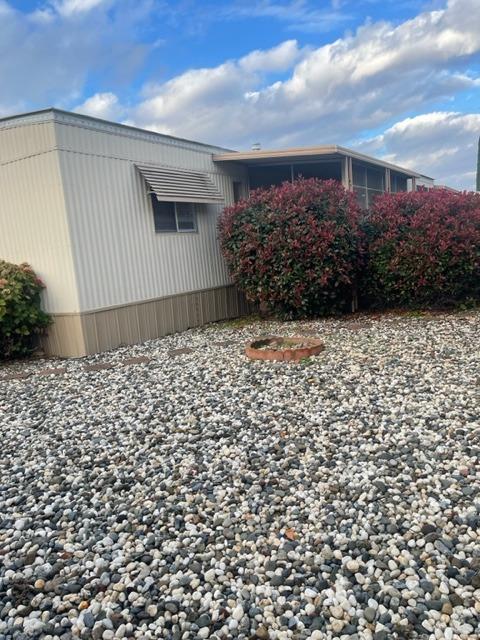 Single-story home with an awning-covered window, red shrubs, and a rock-covered yard.