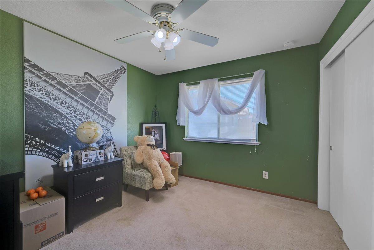 Bedroom with green walls, beige carpet, Eiffel Tower mural, and a chair holding a large teddy bear.