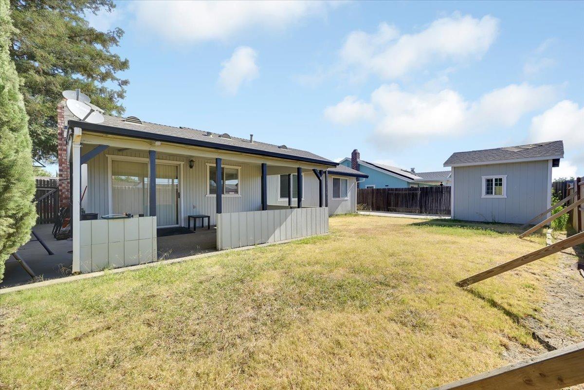 Backyard with a covered patio, fenced lawn, and detached storage shed.