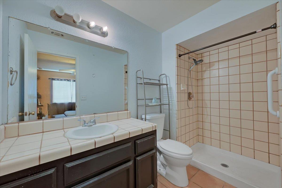 Bathroom with a dark wood vanity, tiled sink counter, toilet, and peach-tiled shower.