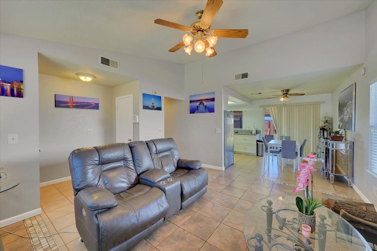 Living room with gray leather reclining sofa, tile floors, and open dining and kitchen area.