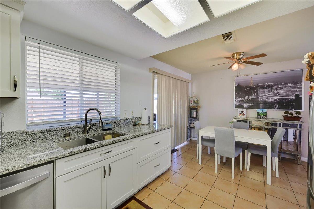 Kitchen with granite counters and white cabinets opening to a tiled dining area.