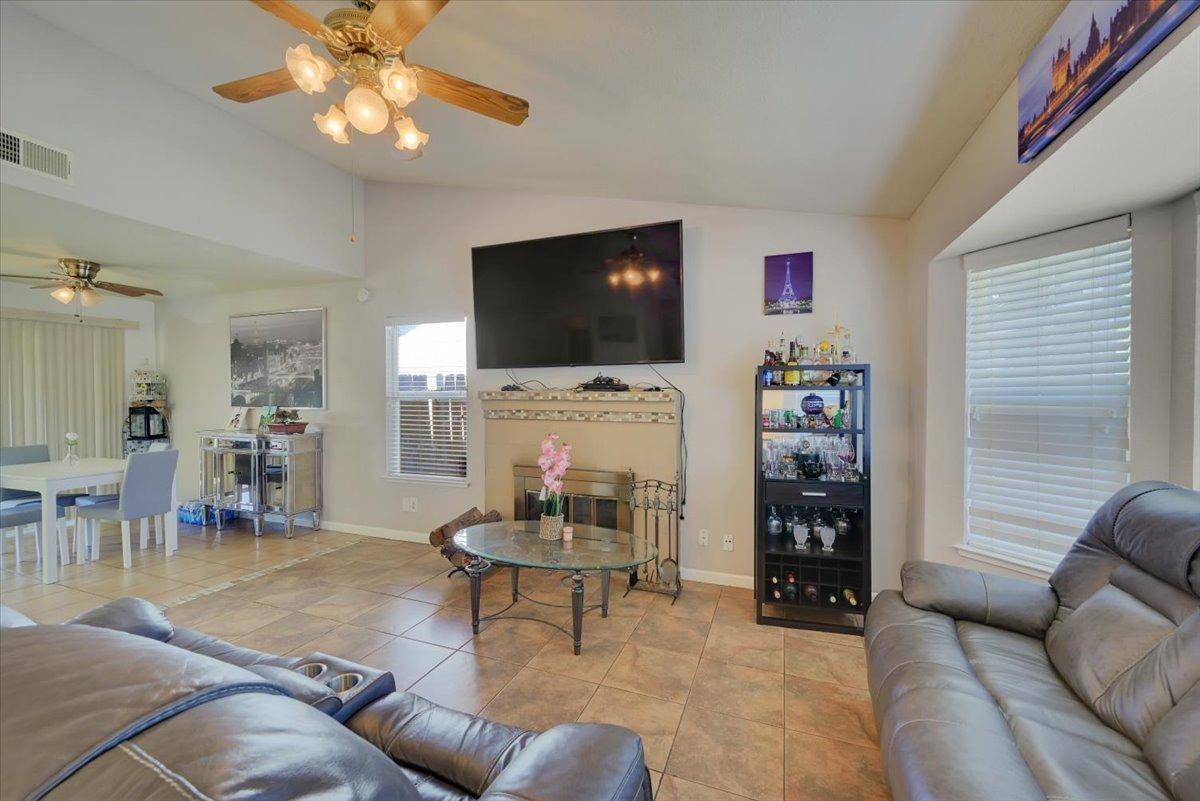 Living room with tan tile floors, leather sofas, and a fireplace beneath a wall-mounted television.