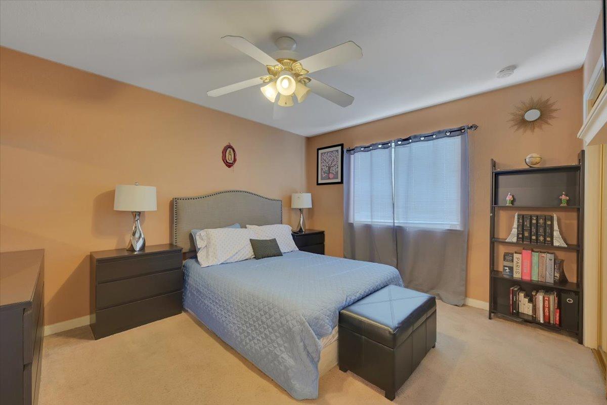 Furnished bedroom with a blue quilted bed, peach walls, and a ceiling fan.
