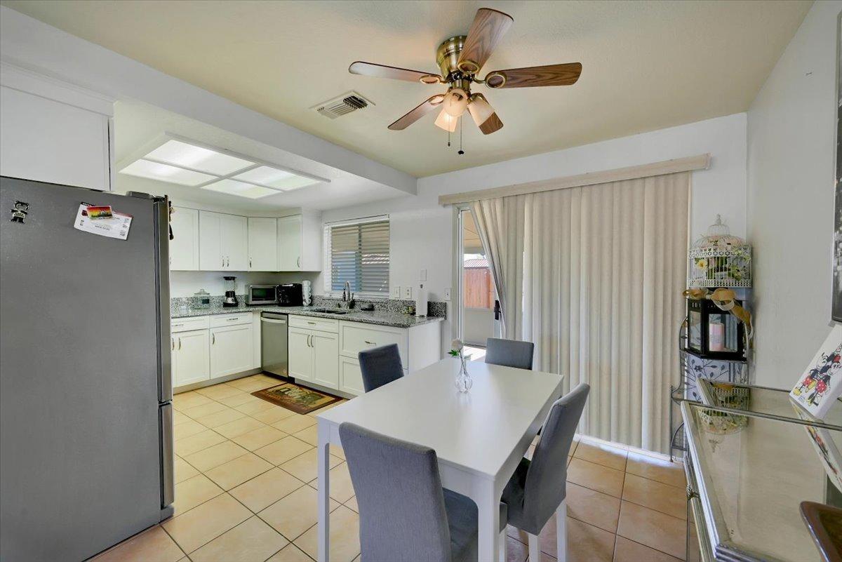 Kitchen and dining area with white cabinets, granite counters, and a dining table beside vertical blinds.