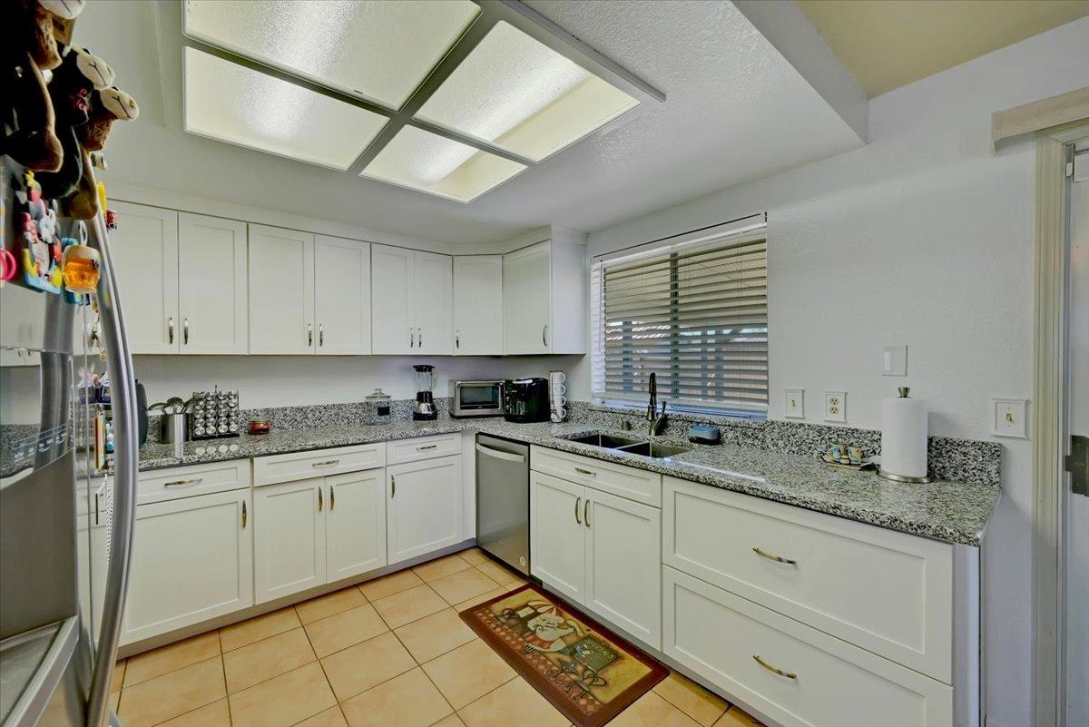 Kitchen with white cabinets, speckled granite counters, stainless appliances, and a sink beneath a window.