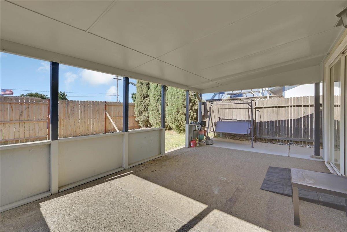 Covered concrete patio with a fenced yard and hanging swing.