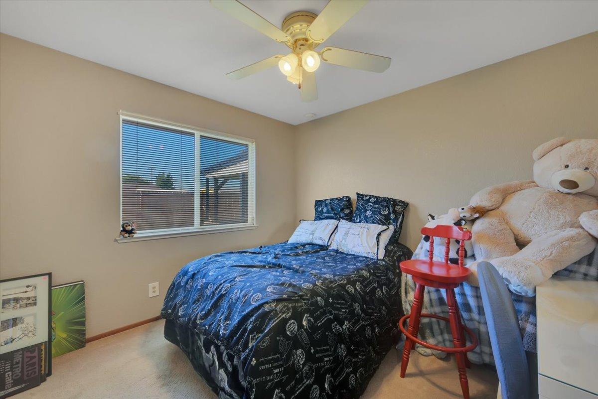 Furnished bedroom with blue patterned bedding, a window with blinds, and oversized teddy bears.