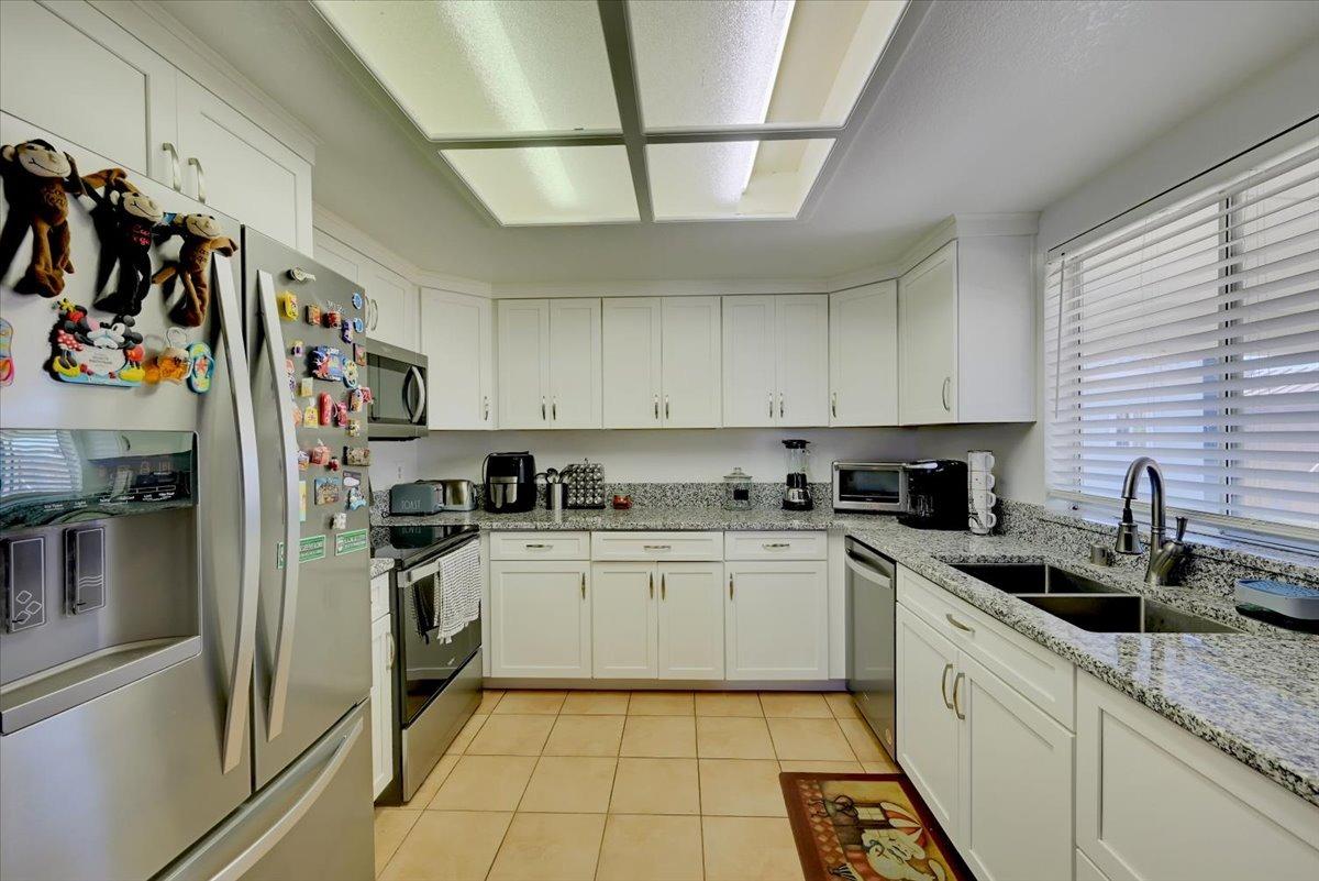 Kitchen with white cabinets, granite counters, stainless appliances, and a double sink beneath a window.