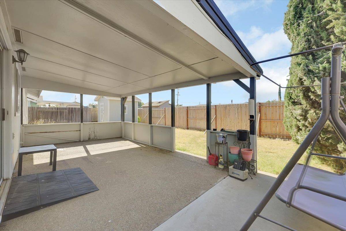 Covered concrete patio with white walls, potted plants, and a fenced backyard.