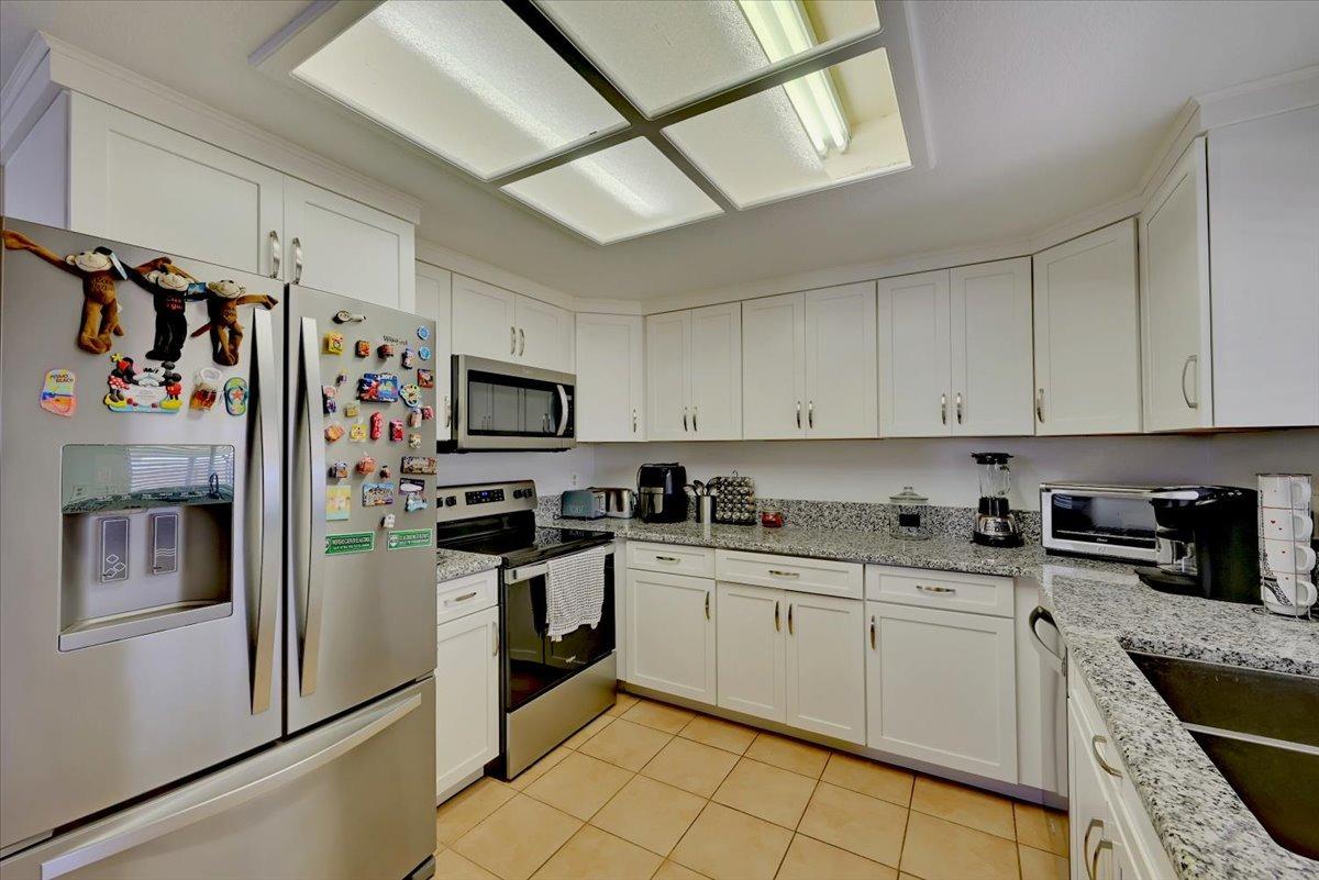 Kitchen with white cabinetry, granite counters, stainless steel appliances, and a refrigerator covered in magnets.