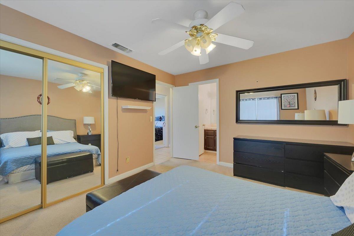 Bedroom with blue quilted bed, mirrored closet doors, ceiling fan, and dark dresser.