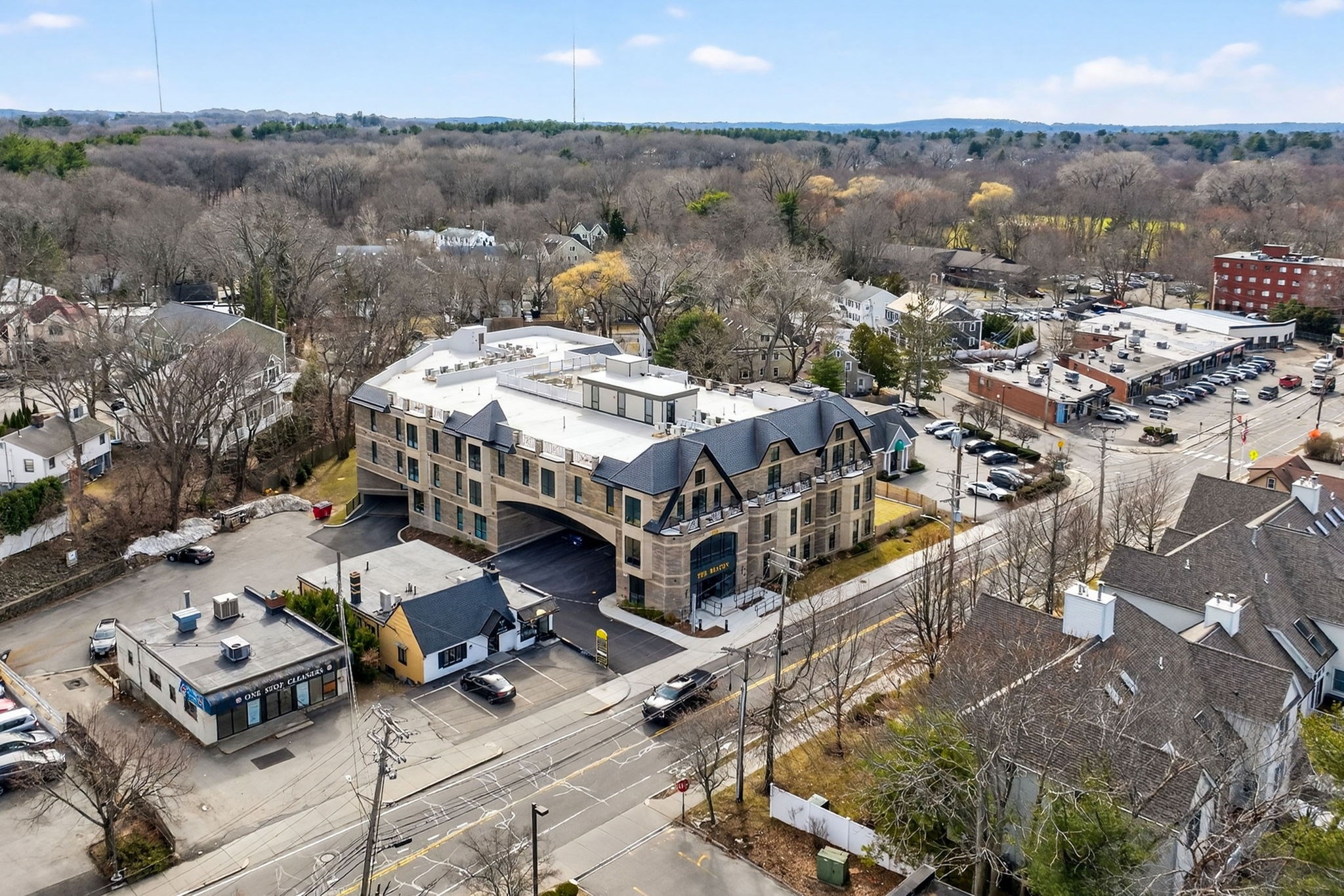 Aerial view of a multi-story condominium building beside a road and neighborhood businesses.