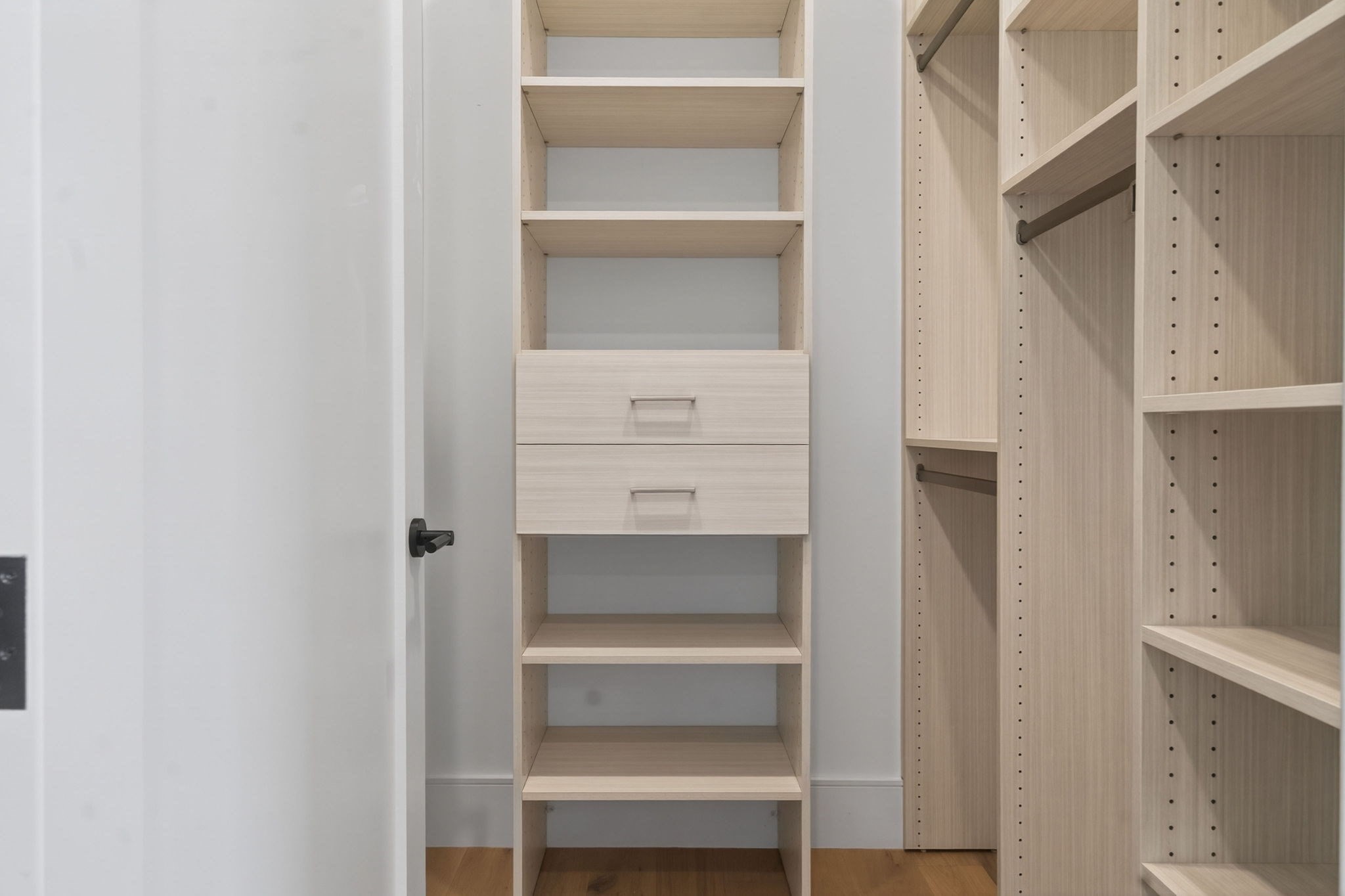 Walk-in closet with light wood shelving, two central drawers, and hanging rods.