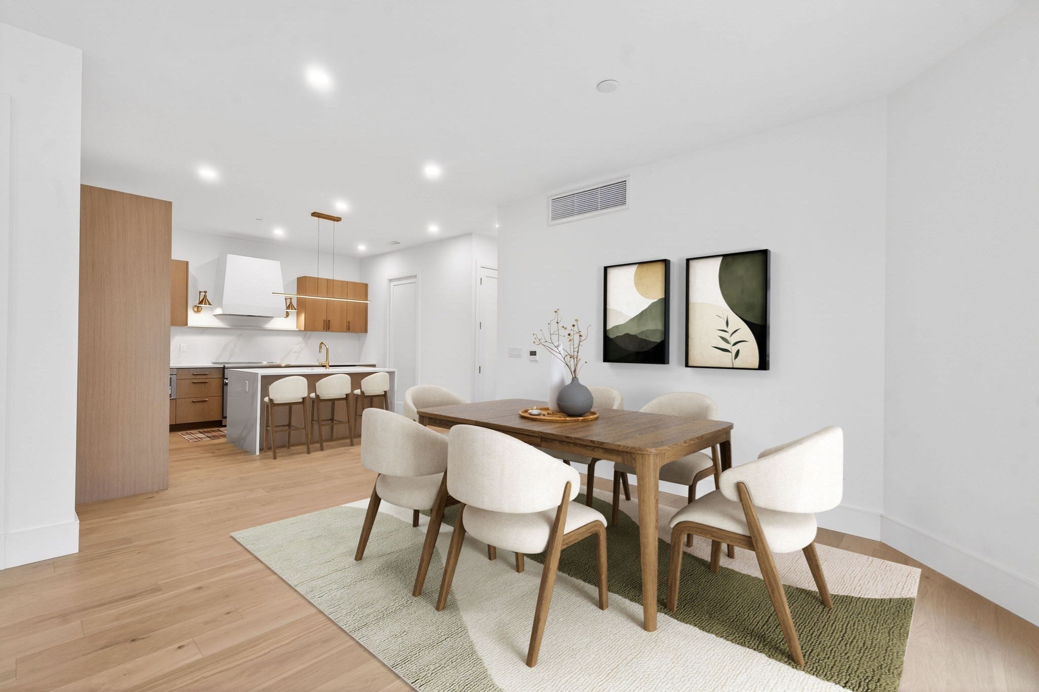 Open-plan dining area with a wood table and cream chairs beside a modern kitchen with warm wood cabinetry.