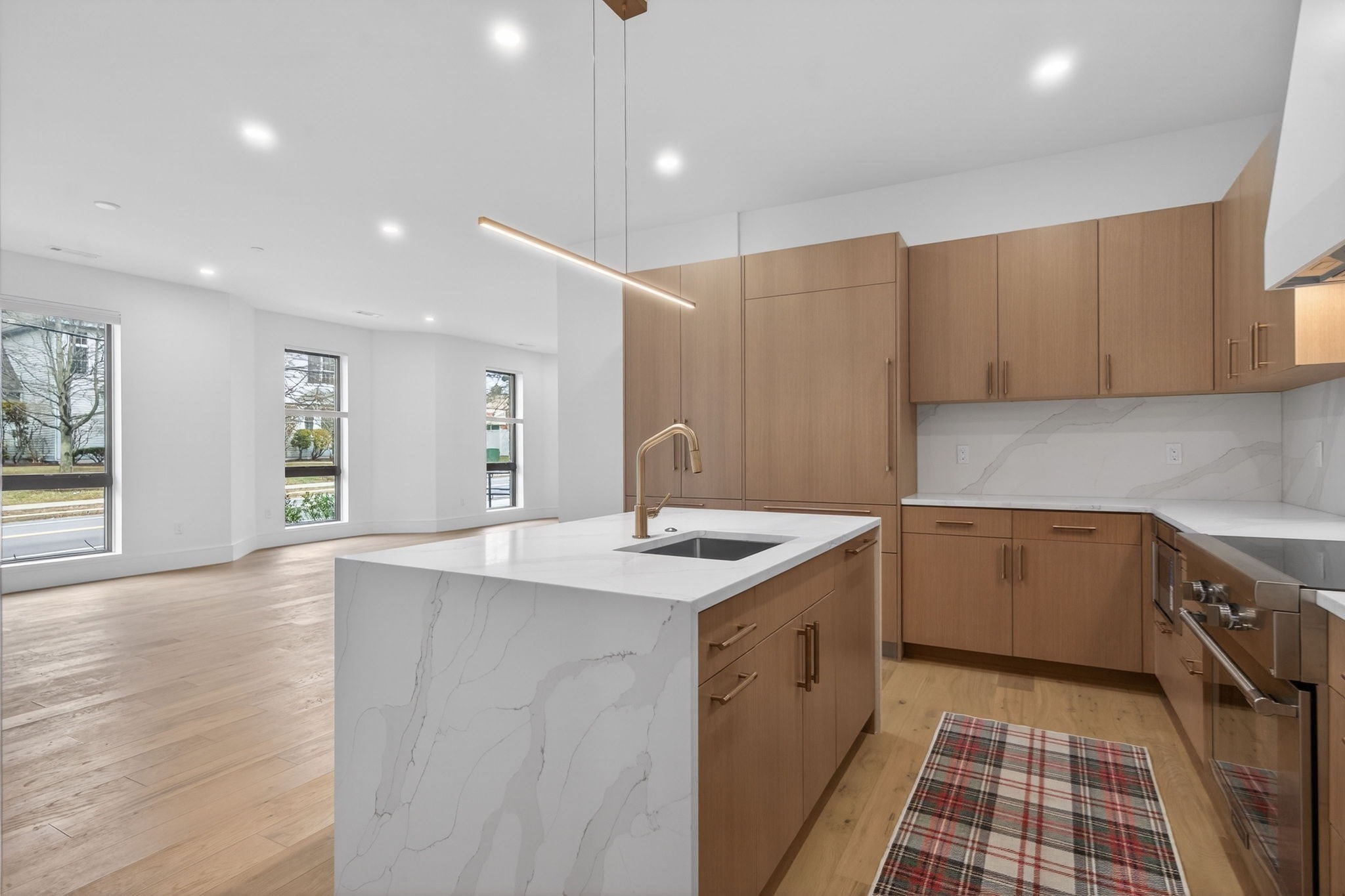 Modern kitchen with a veined-stone island, warm wood cabinets, and windows along the open living area.