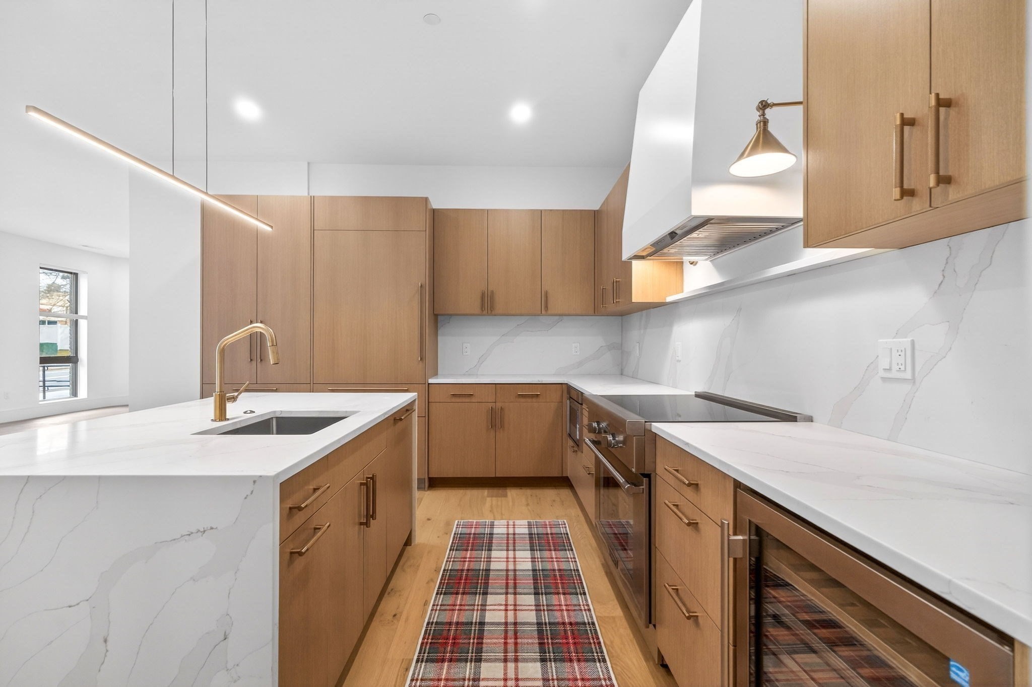 Modern kitchen with warm wood cabinetry, veined white counters, a large island, and a plaid runner.