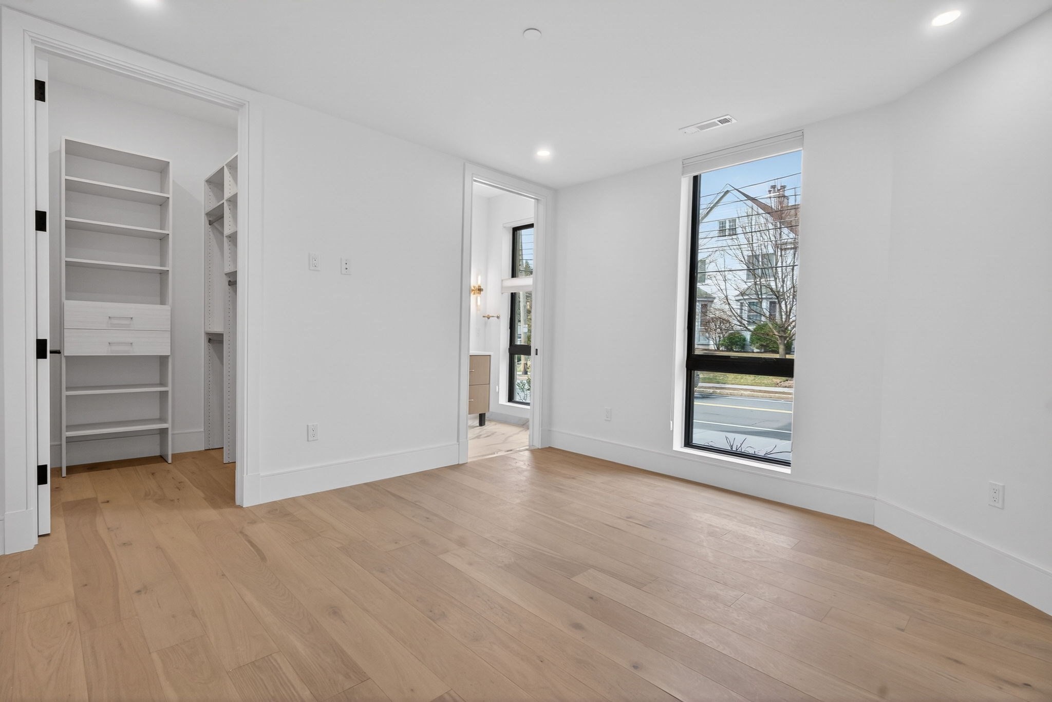 Bright empty room with hardwood floors, built-in closet shelving, and a large window.