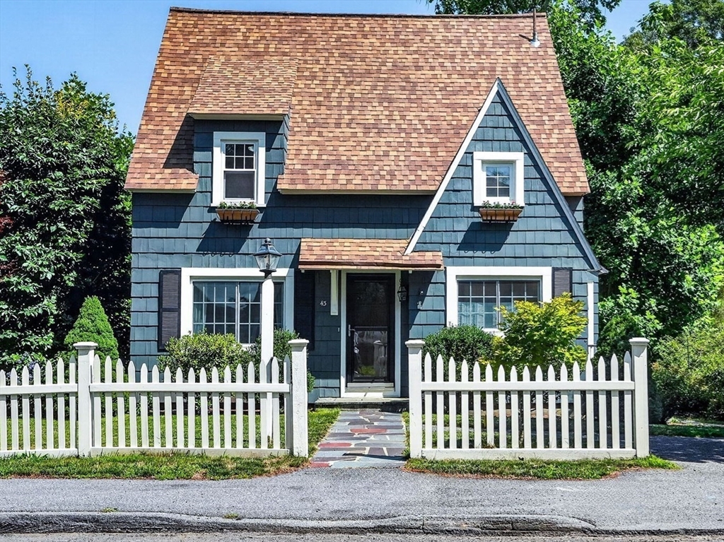 Blue-shingled house with a steep roof, white picket fence, and stone walkway to the entrance.