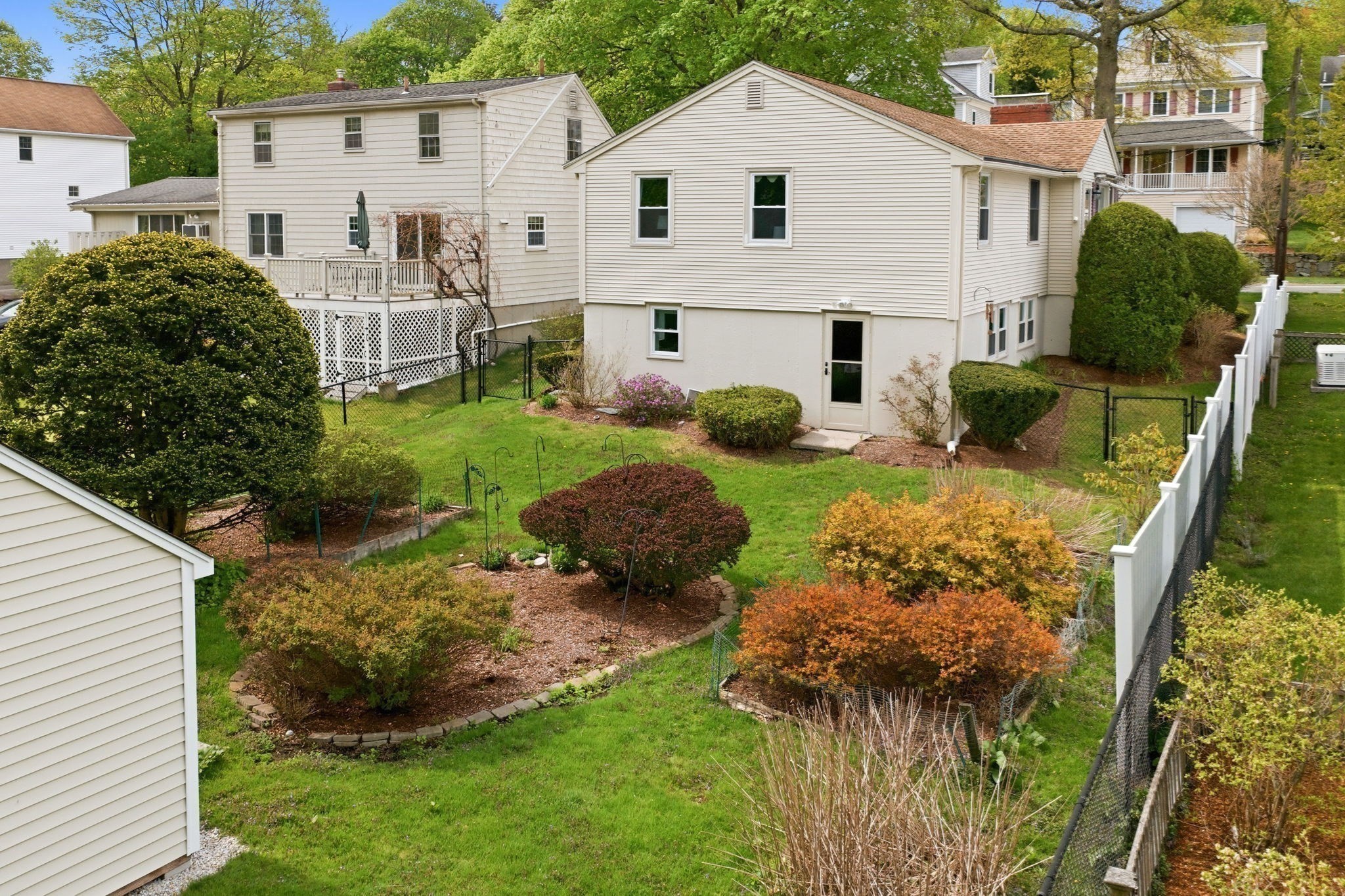 House viewed from the backyard, with a fenced lawn, landscaped garden beds, and mature shrubs.