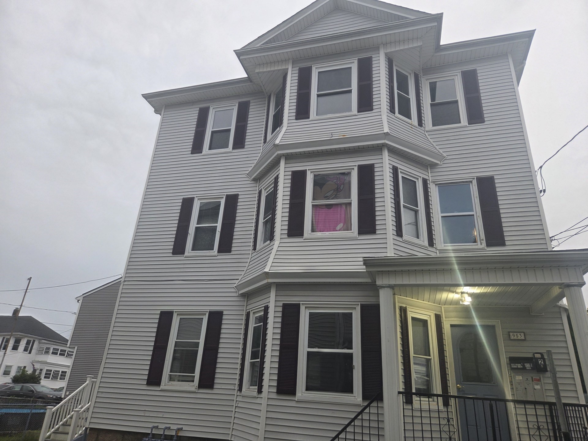 Tall gray-sided house with projecting bay windows and a lit covered front porch.