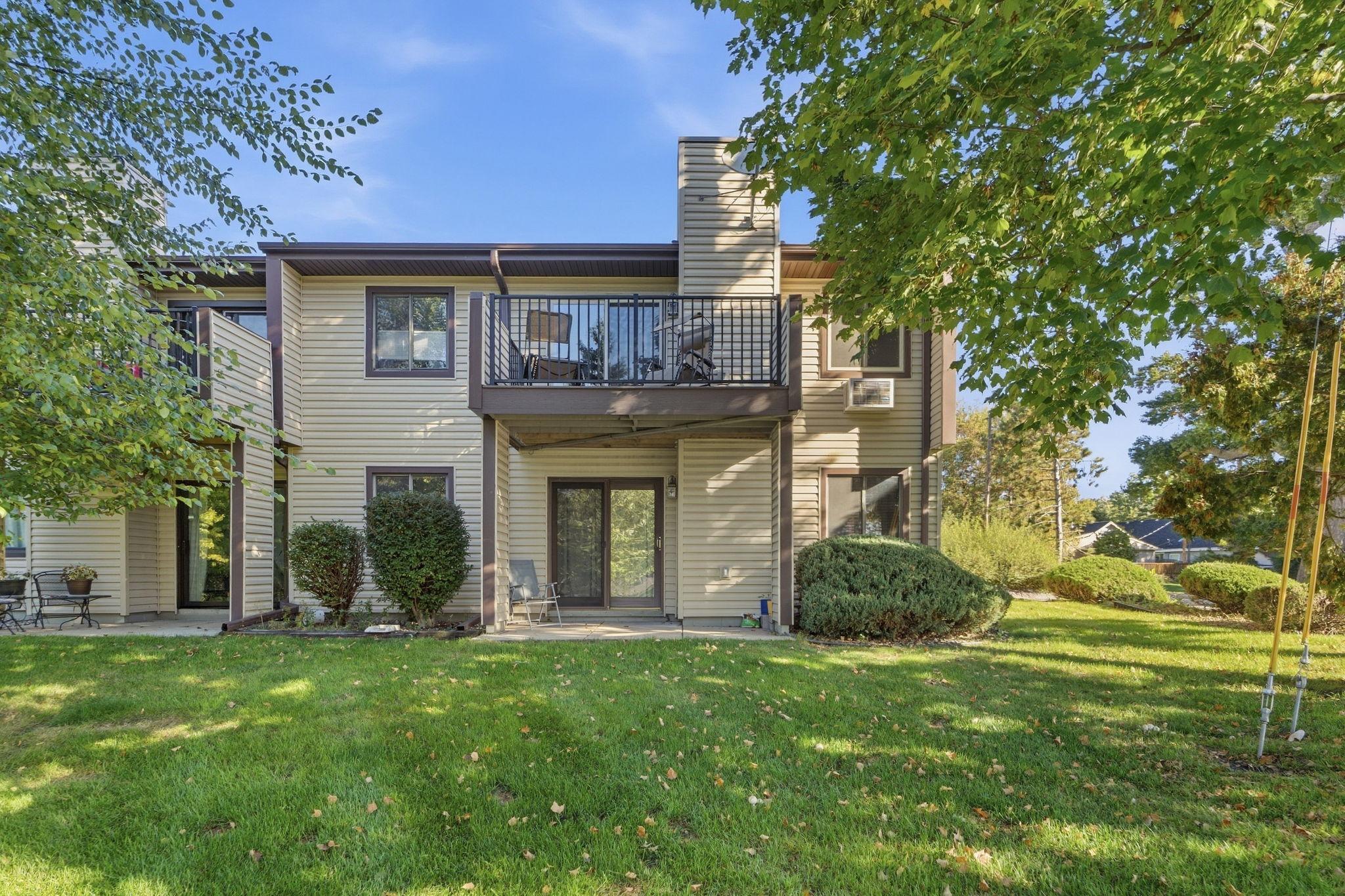 Home’s rear exterior with an elevated balcony, patio, and landscaped lawn.