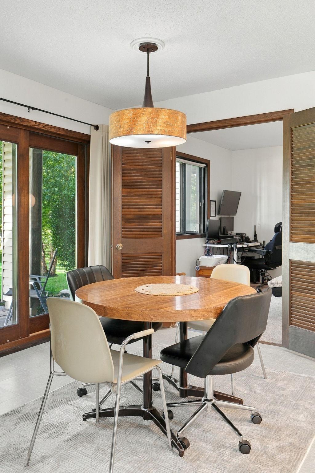 Dining area with a round wooden table, pendant light, patio doors, and an adjoining home office.