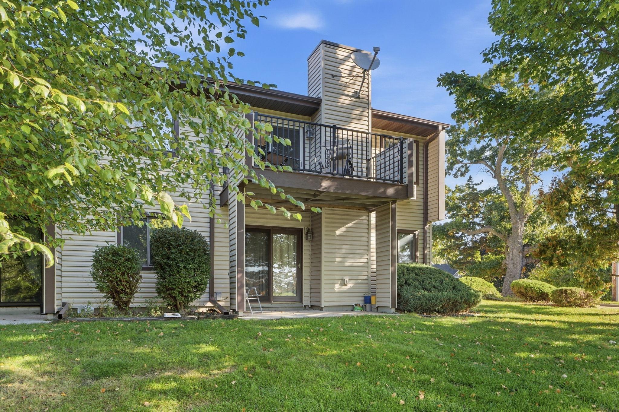 Home’s rear exterior with a raised black-railed deck, sliding doors, and mature trees.