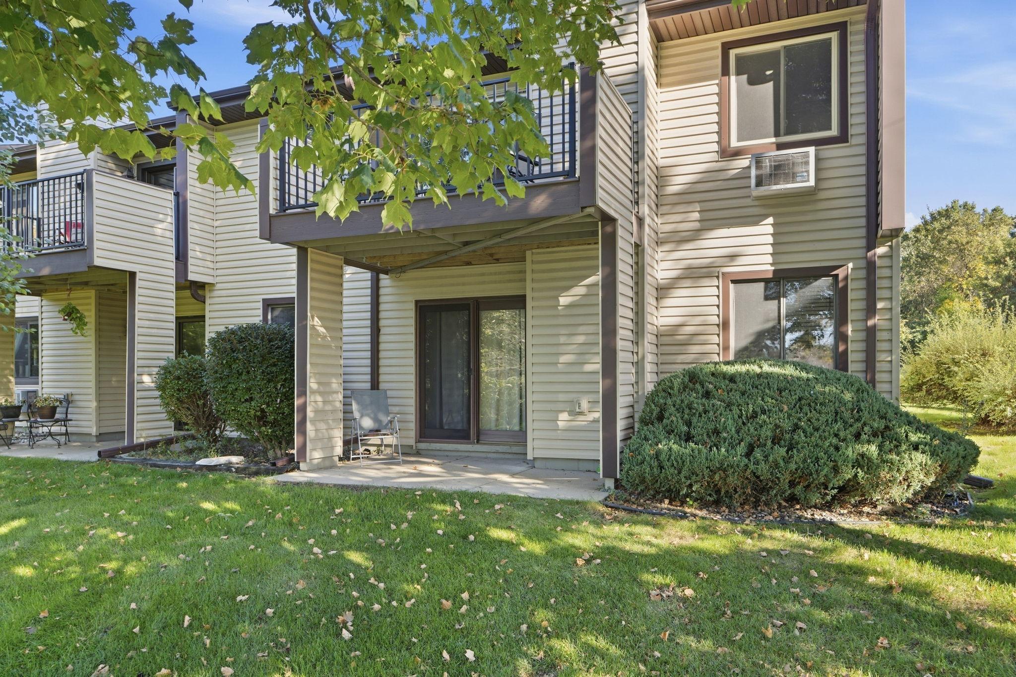 Beige-sided residence with balconies, covered patios, and shrubs along the lawn.