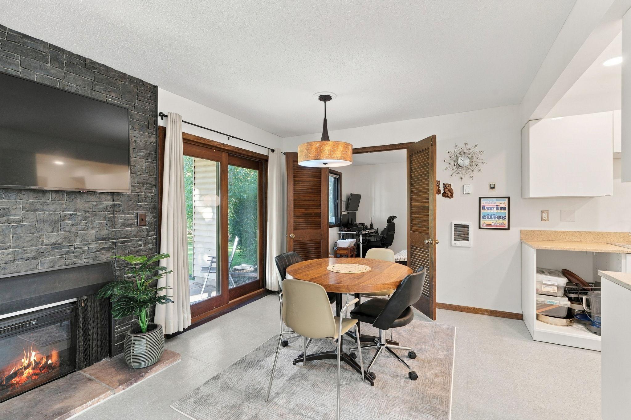 Dining area with a round wooden table beside a stone fireplace and sliding glass doors.
