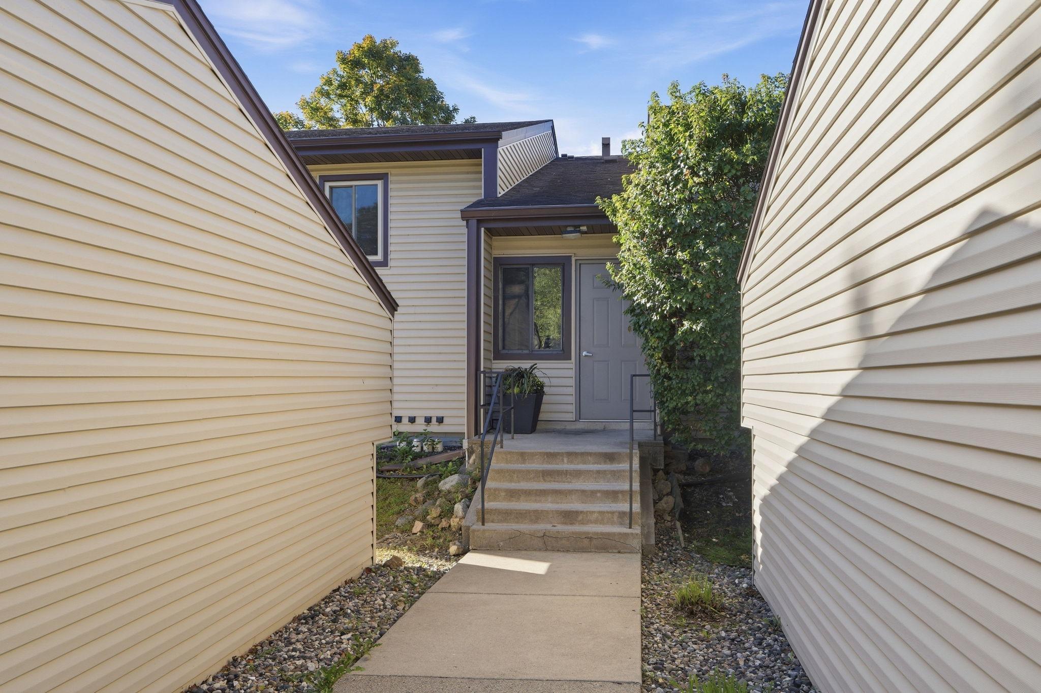 Home entrance with a gray door, concrete steps, and a leafy tree beside cream siding.