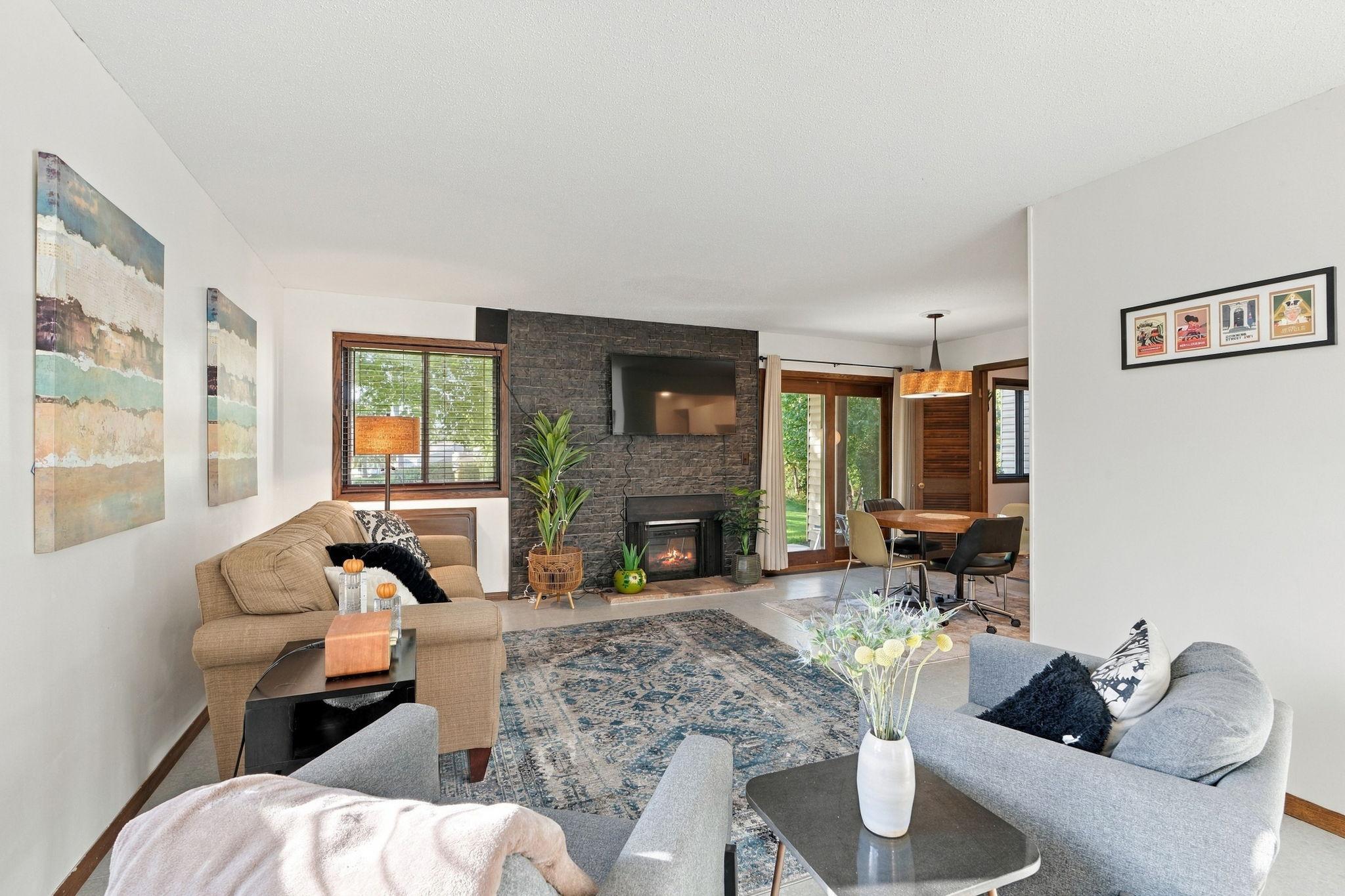 Living room with a stone fireplace, mounted TV, and adjoining dining area.
