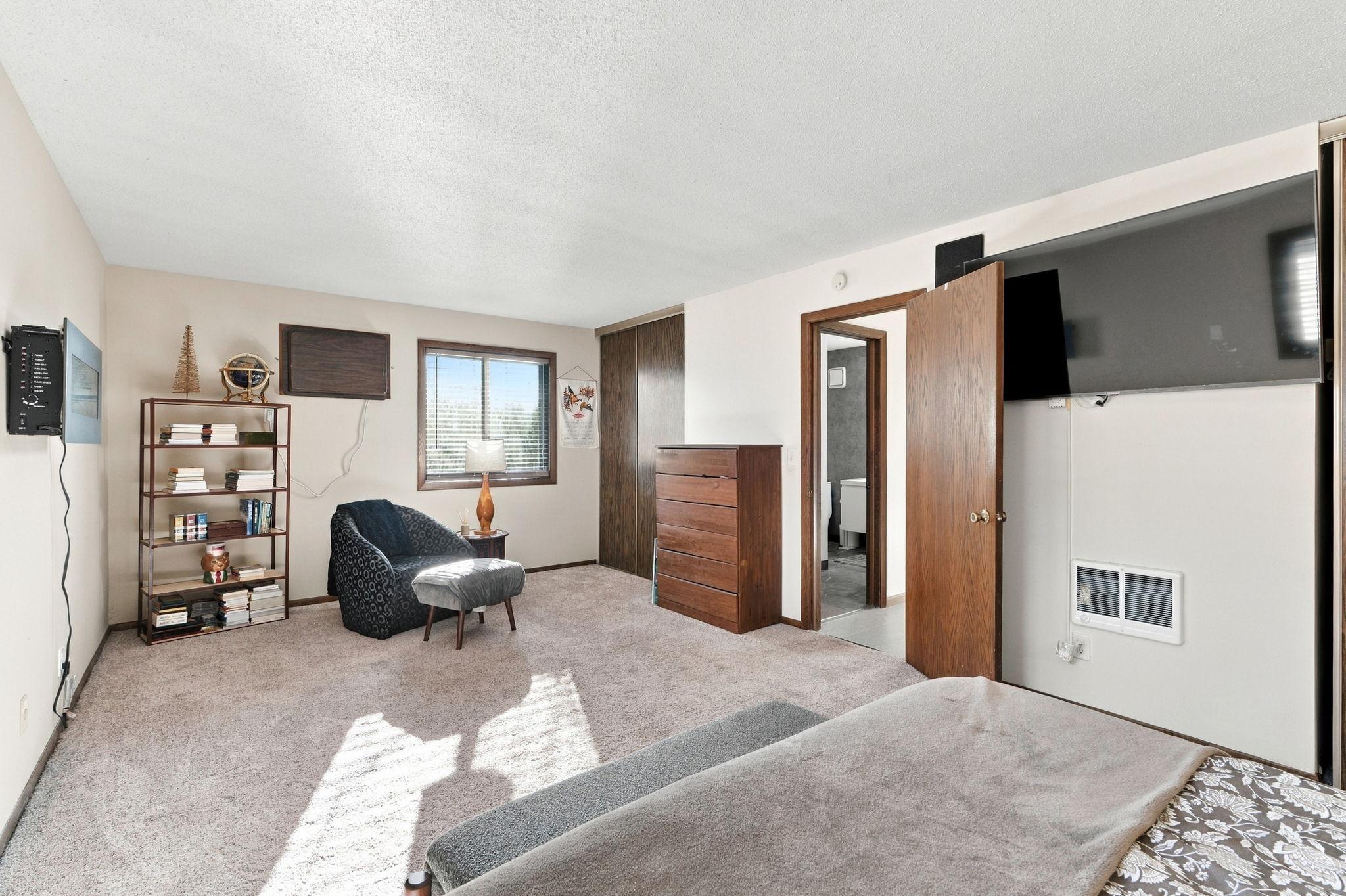Bedroom with a bed, wooden dresser, bookcase, and open doorway to a bathroom.