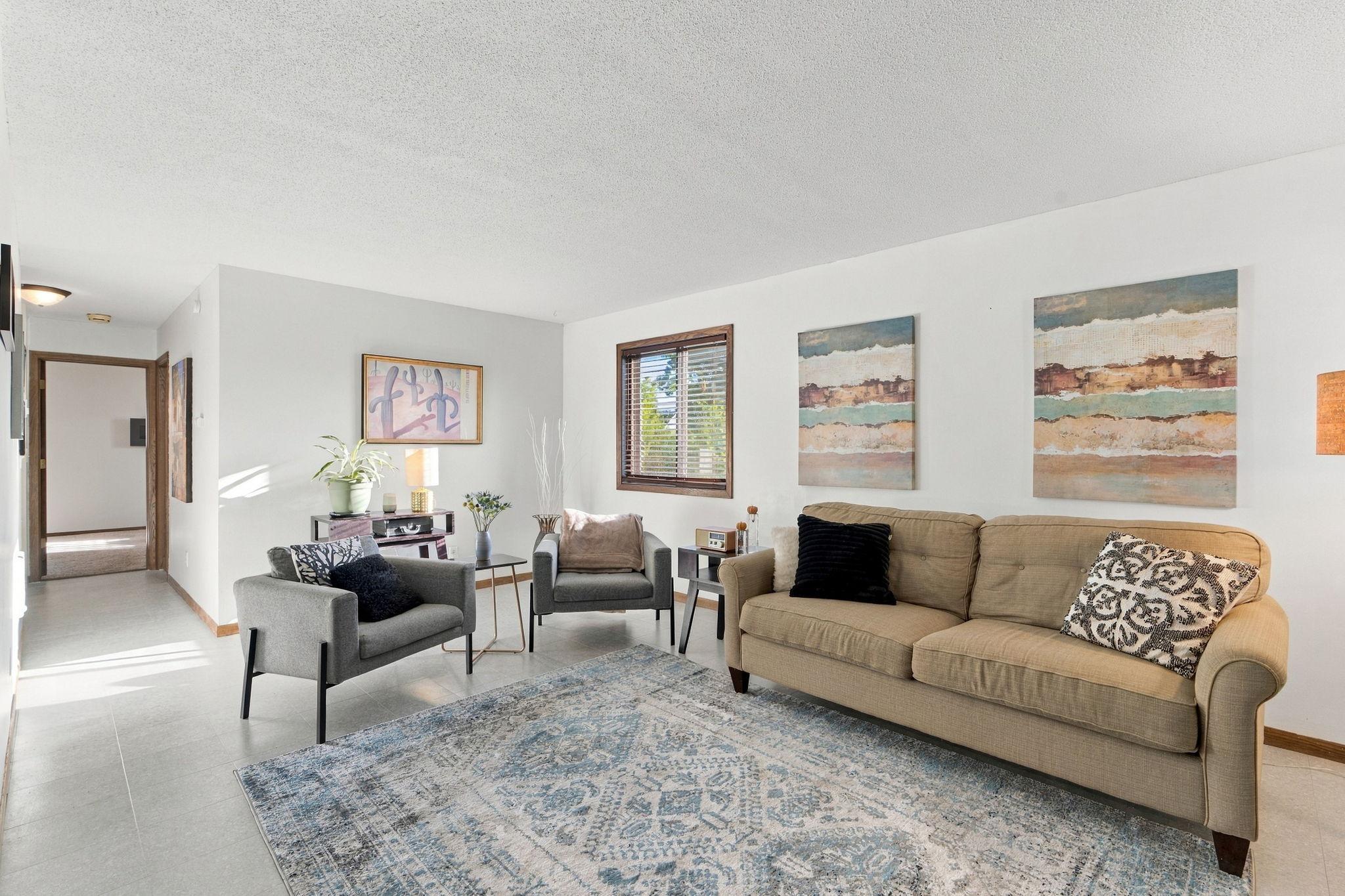 Living room with a tan sofa, gray armchairs, and a blue patterned rug.