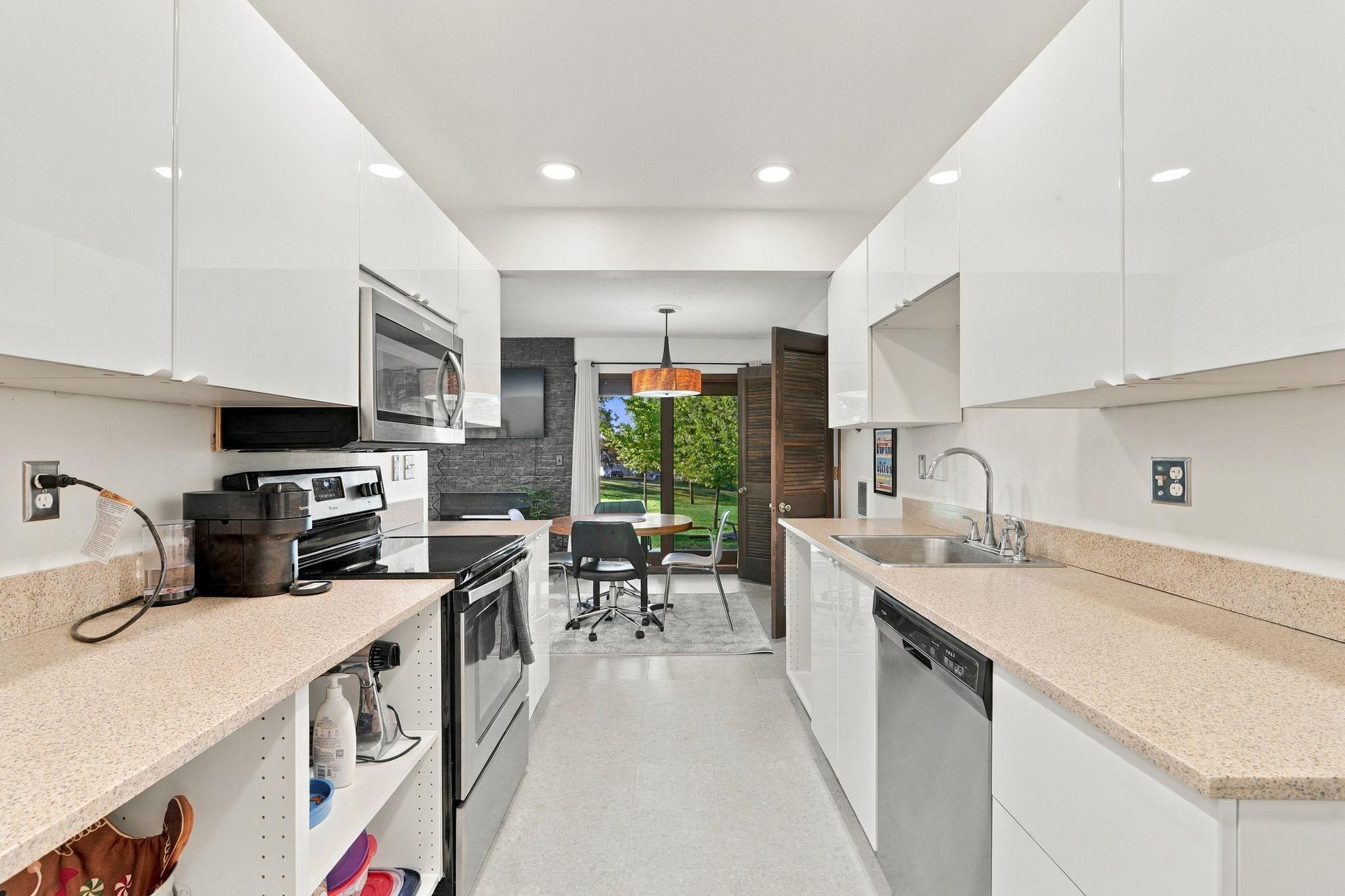 Modern kitchen with white cabinets, speckled counters, stainless appliances, and a dining nook by an open door.