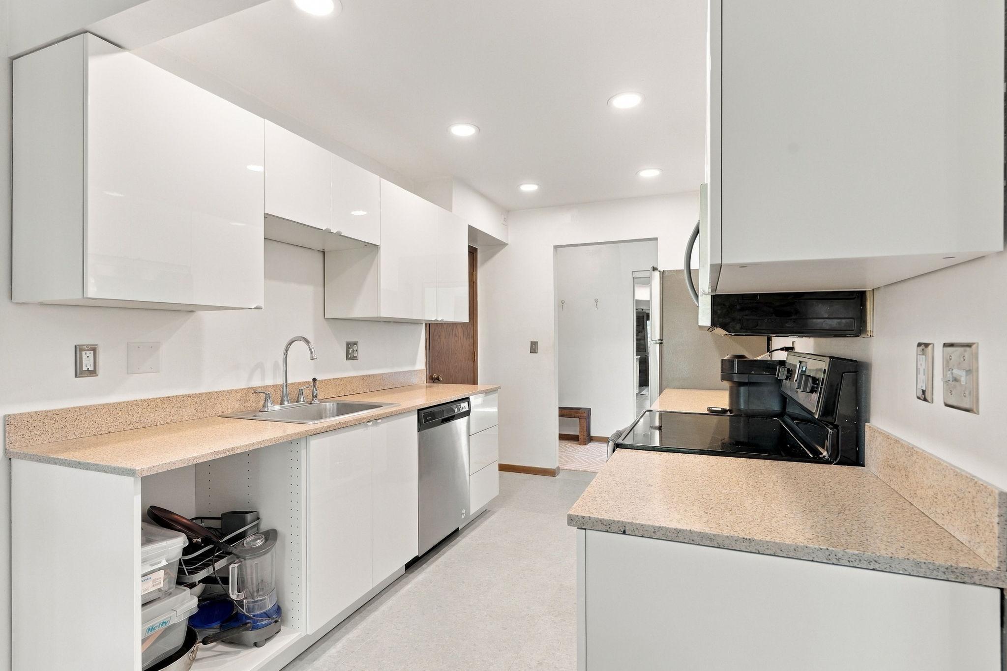 Kitchen with glossy white cabinets, speckled countertops, stainless dishwasher, and black electric range.