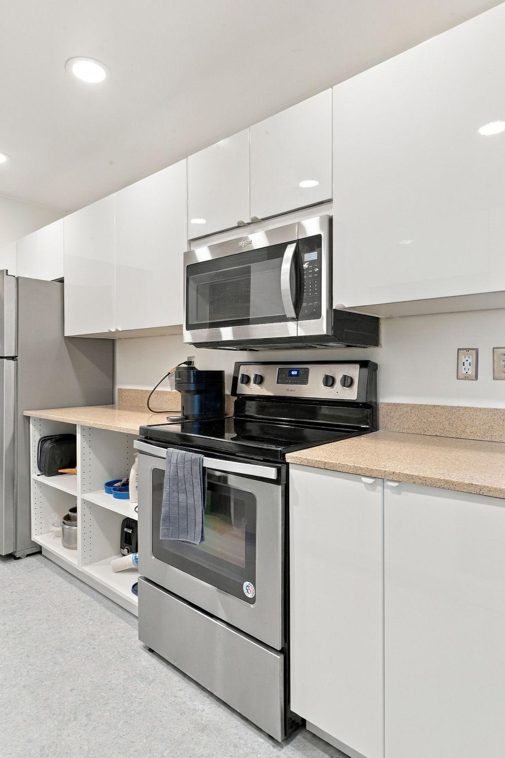 Kitchen with glossy white cabinets, stainless steel appliances, and open shelving beneath the counter.