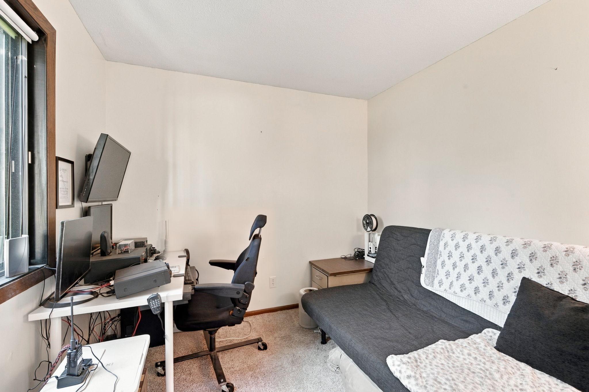 Home office with a computer workstation, office chair, and gray futon beside a large window.