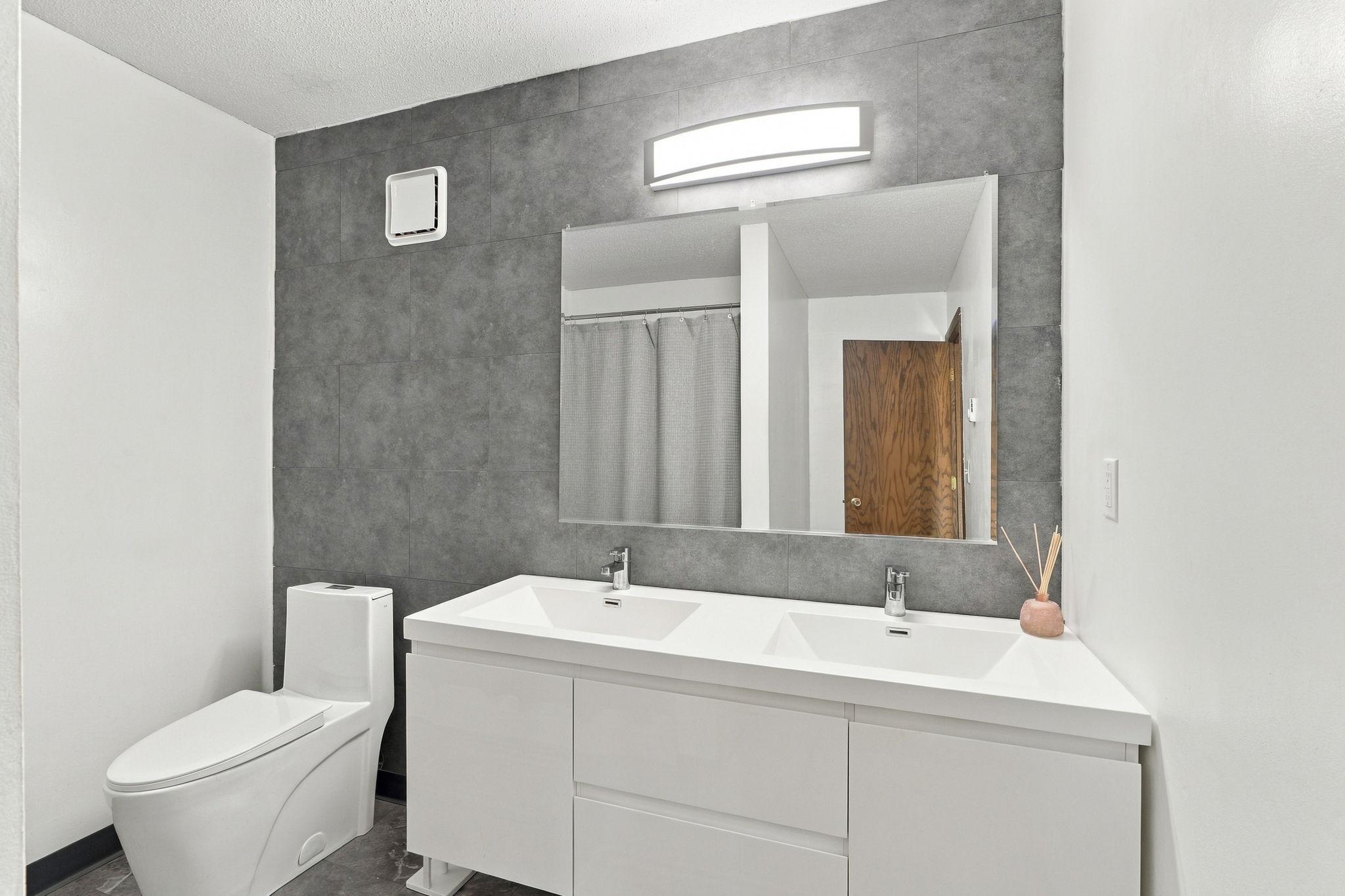 Bathroom with a floating double-sink vanity, large mirror, and gray tile accent wall.