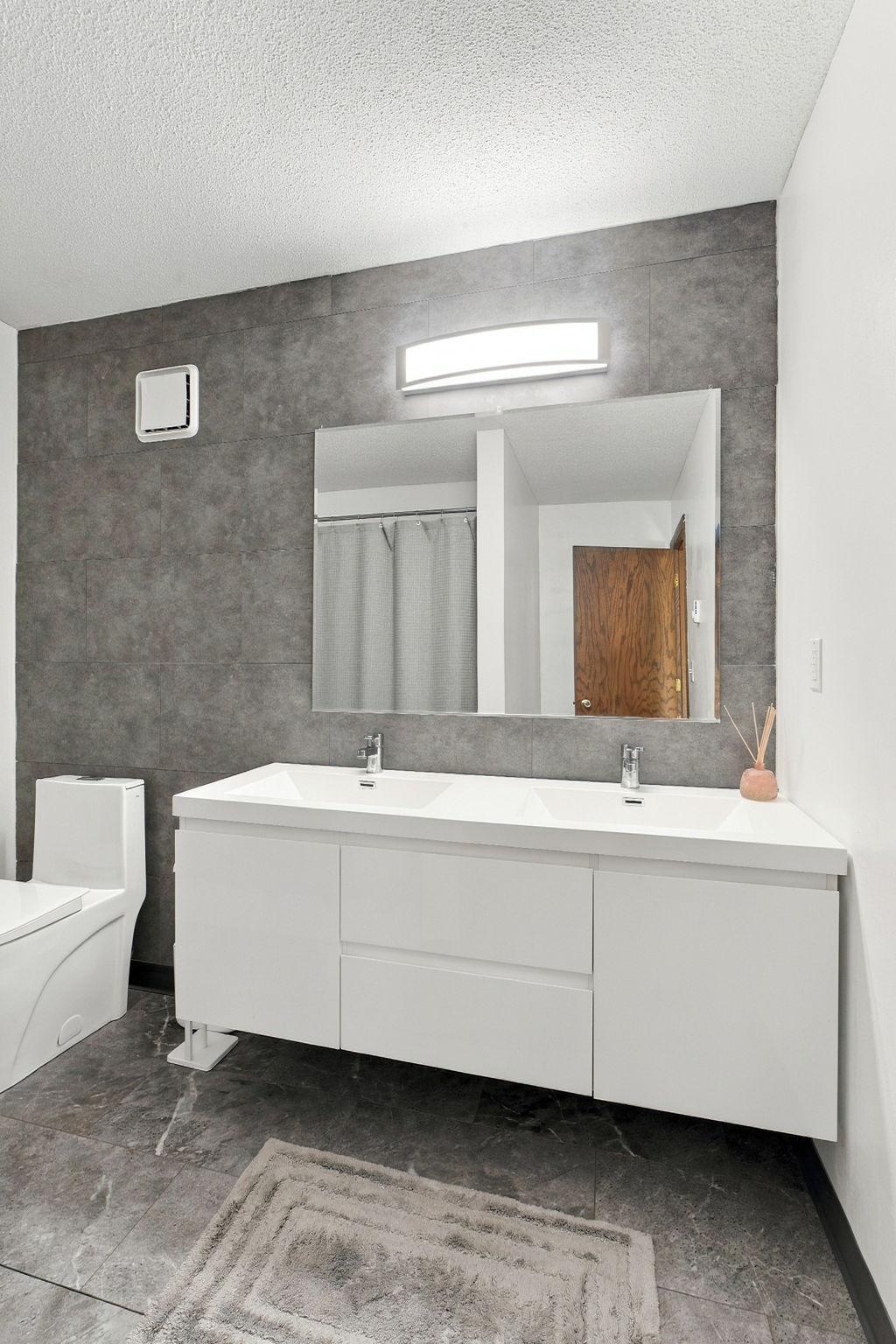 Bathroom with a white double vanity, large mirror, and dark gray tile.