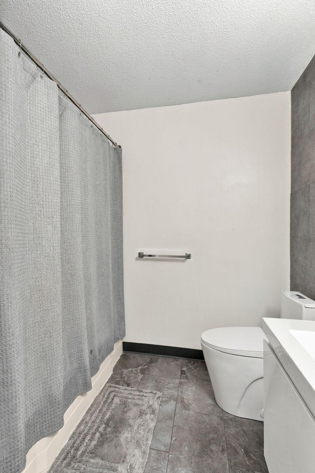 Bathroom with a gray shower curtain, white toilet, and gray tile flooring.