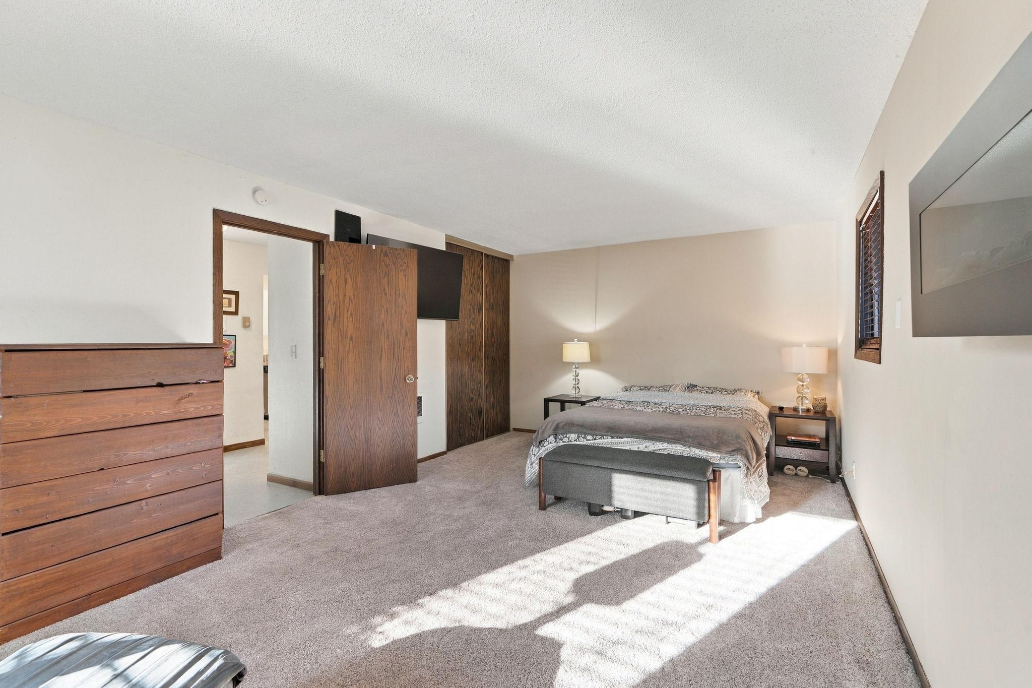 Bedroom with a bed, wooden dresser, and sunlight falling across the carpet.