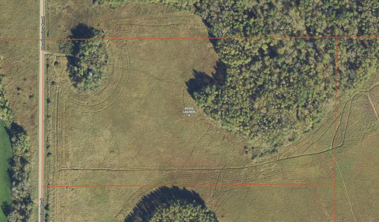 Aerial view of a rural parcel with open grassland, wooded areas, and red boundary lines.