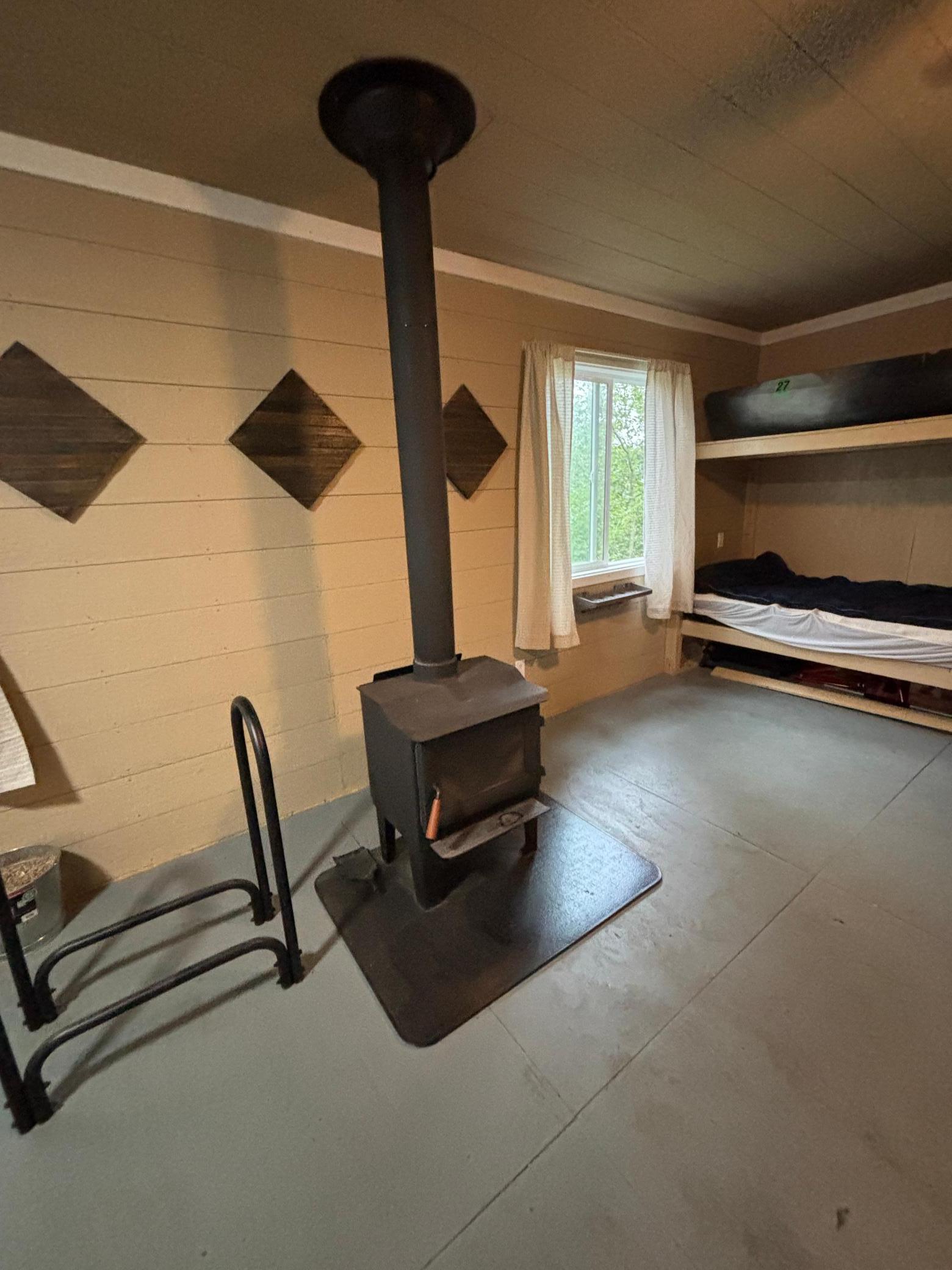 Rustic bedroom with a wood-burning stove, curtained window, and built-in bunk beds.