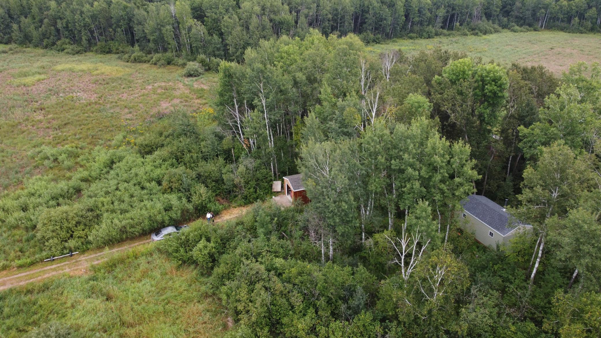 Aerial view of wooded land with grassy clearings, a red outbuilding, and a driveway.