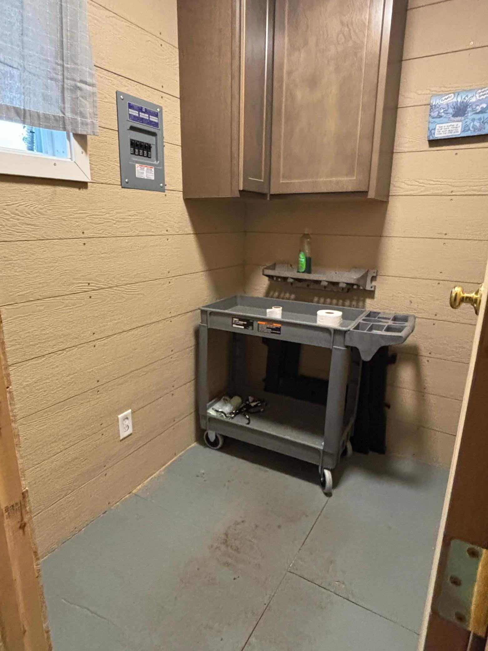 Utility room with a wall cabinet, electrical panel, and rolling work cart.