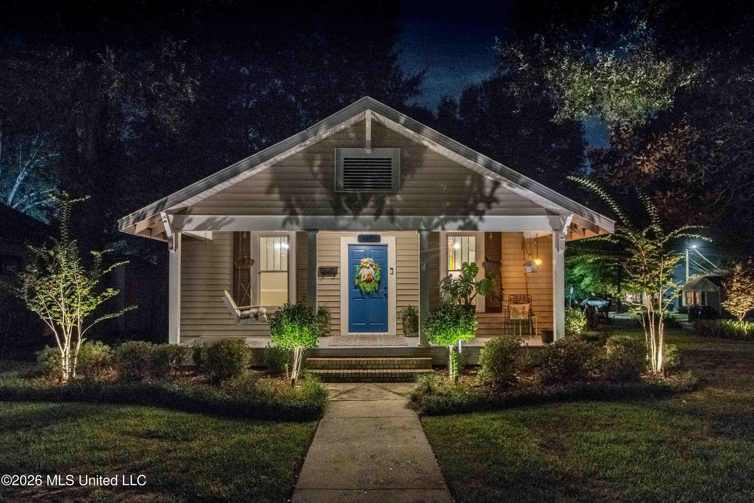 Single-story home at night with a blue front door, covered porch, and illuminated landscaping.