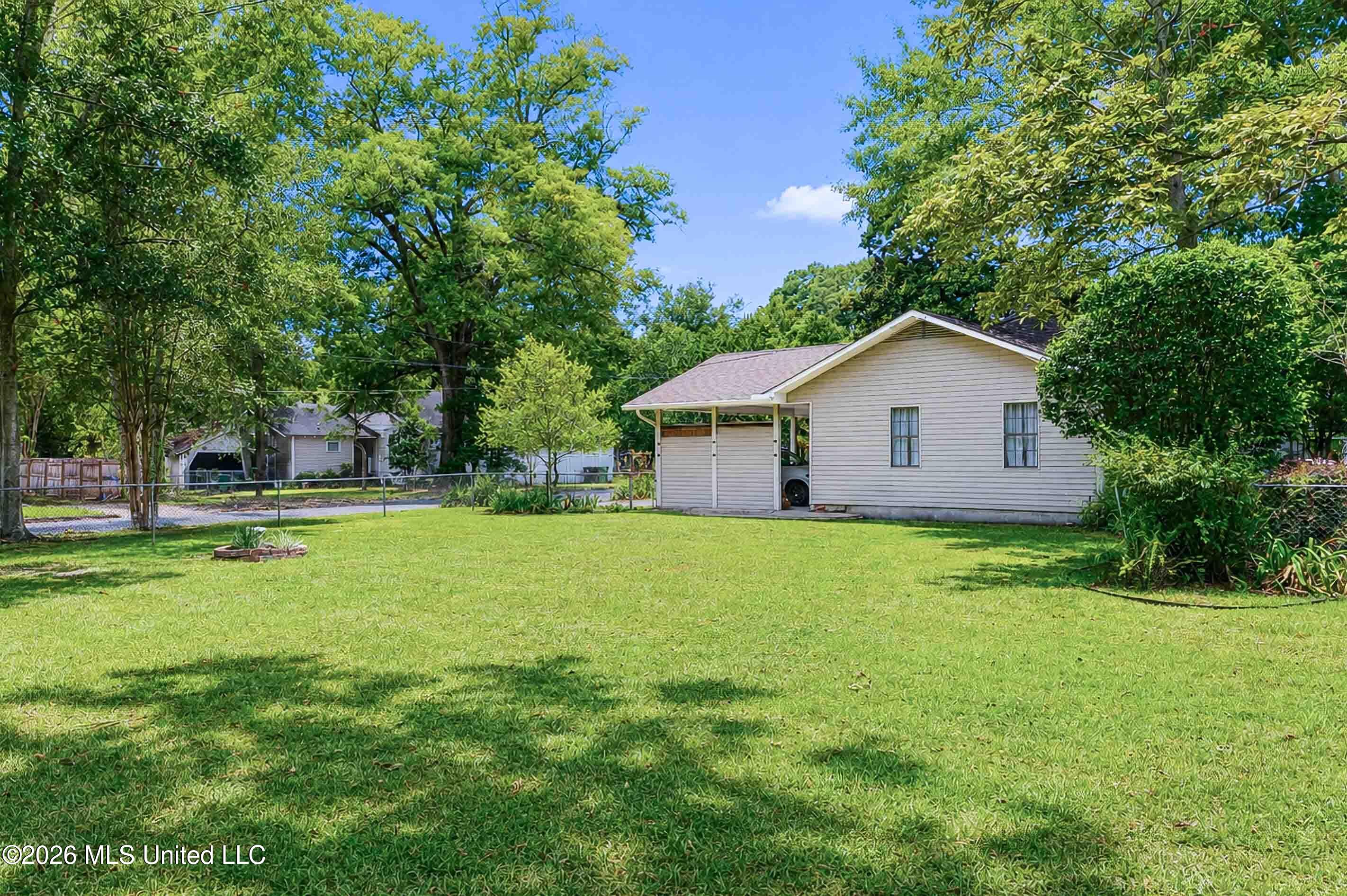 House with a covered carport and spacious grassy yard shaded by mature trees.