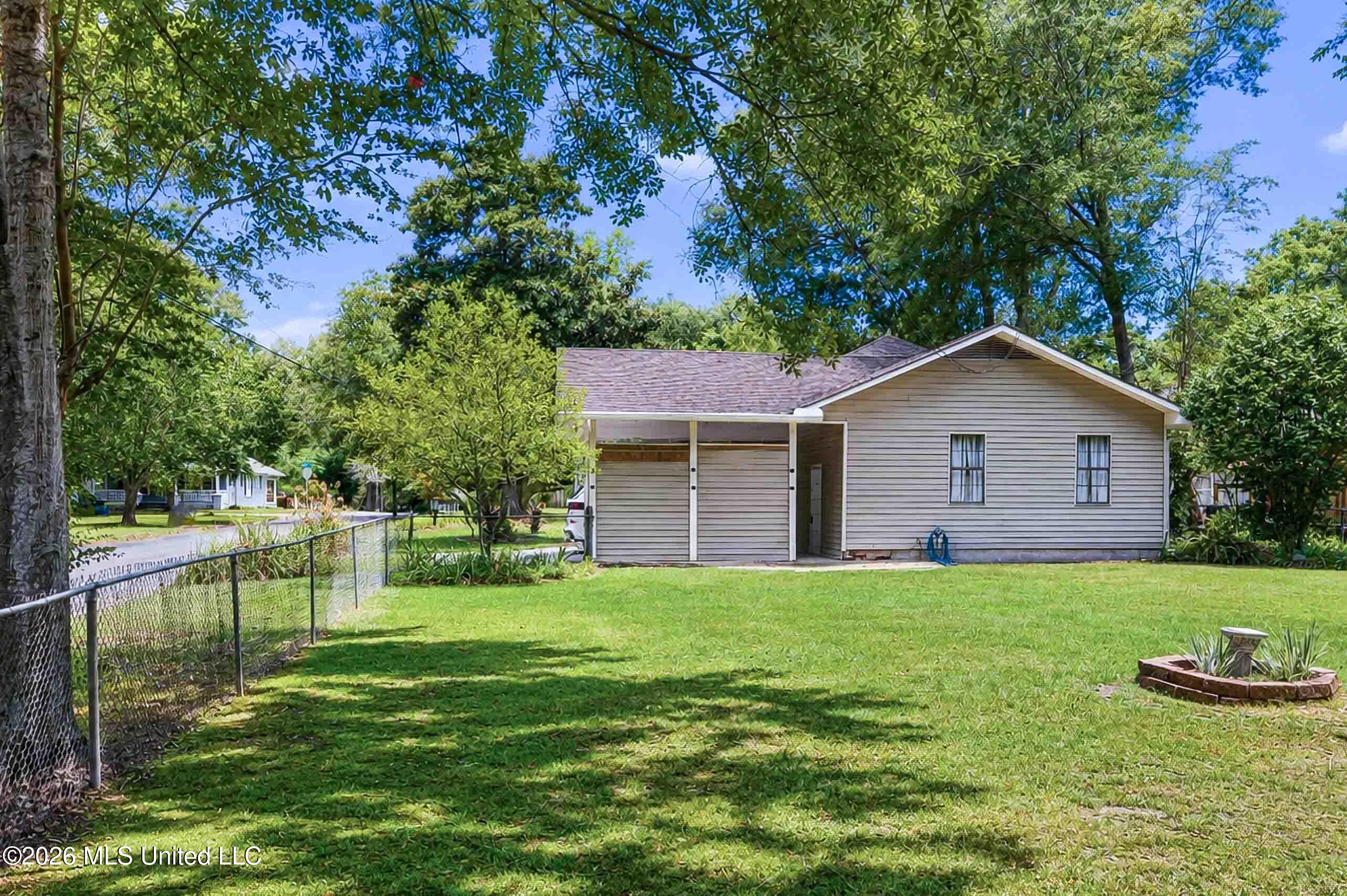 Single-story home with an attached carport beside a broad lawn shaded by mature trees.
