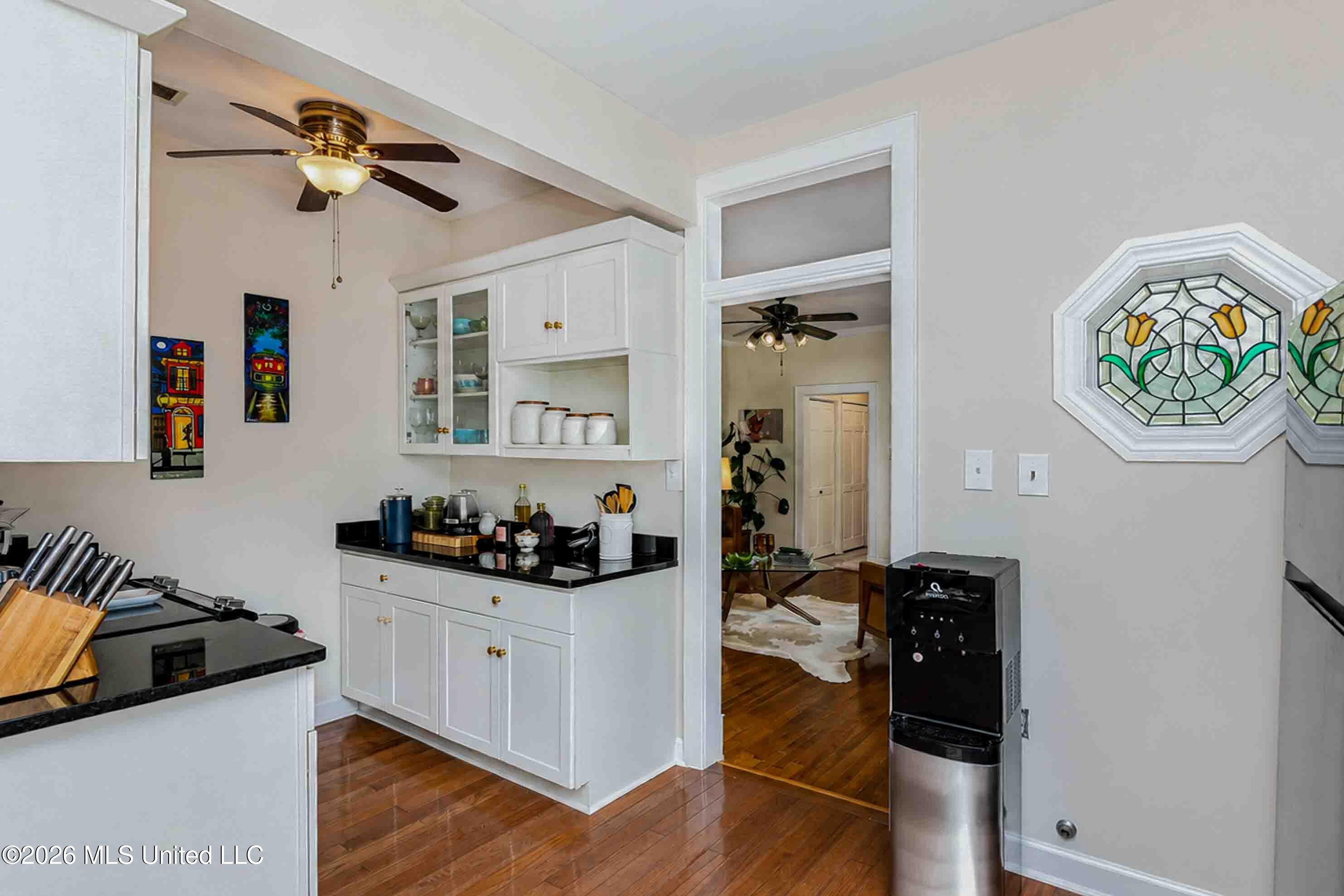 Kitchen with white cabinetry, black countertops, hardwood floors, and a stained-glass tulip window.